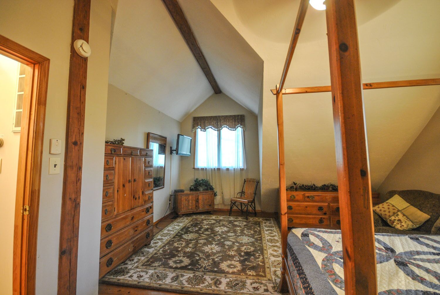 Un dormitorio con cama con dosel, muebles de madera, un televisor y una alfombra estampada.
