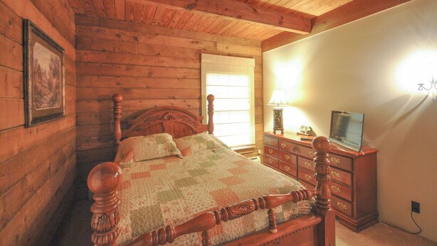 A wooden cabin bedroom with a bed, dresser, and a television on a dresser. - Corey Cabin - Cozy Getaway Minutes from Ohiopyle (Ohiopyle)
