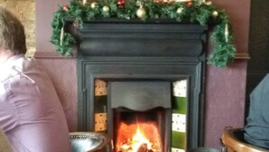 Una chimenea con un adorno navideño, una alfombra estampada y una pared de piedra.