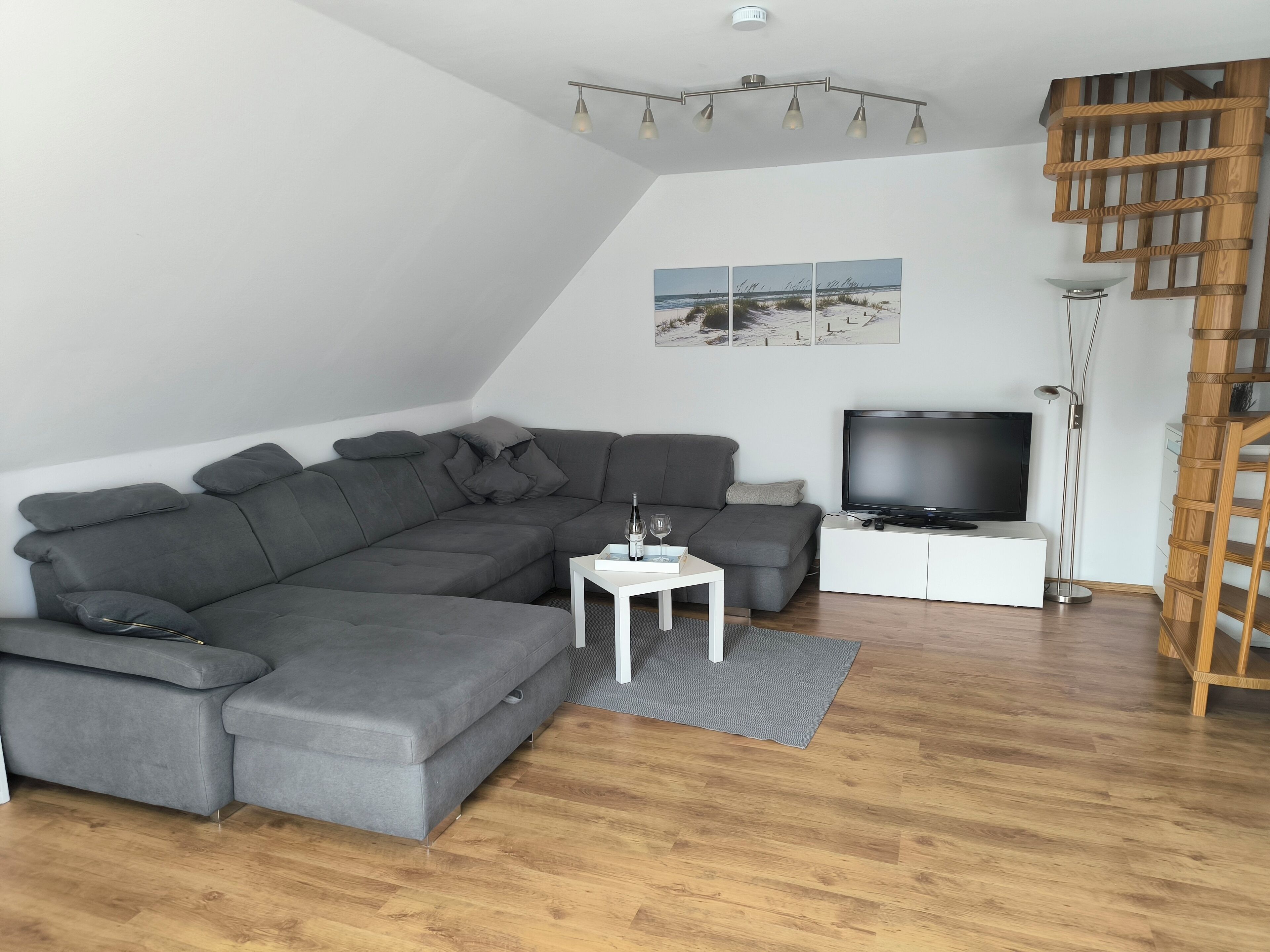 A modern living room with a grey sectional sofa, a flat-screen TV, a small white table, and a wooden ladder against the wall.