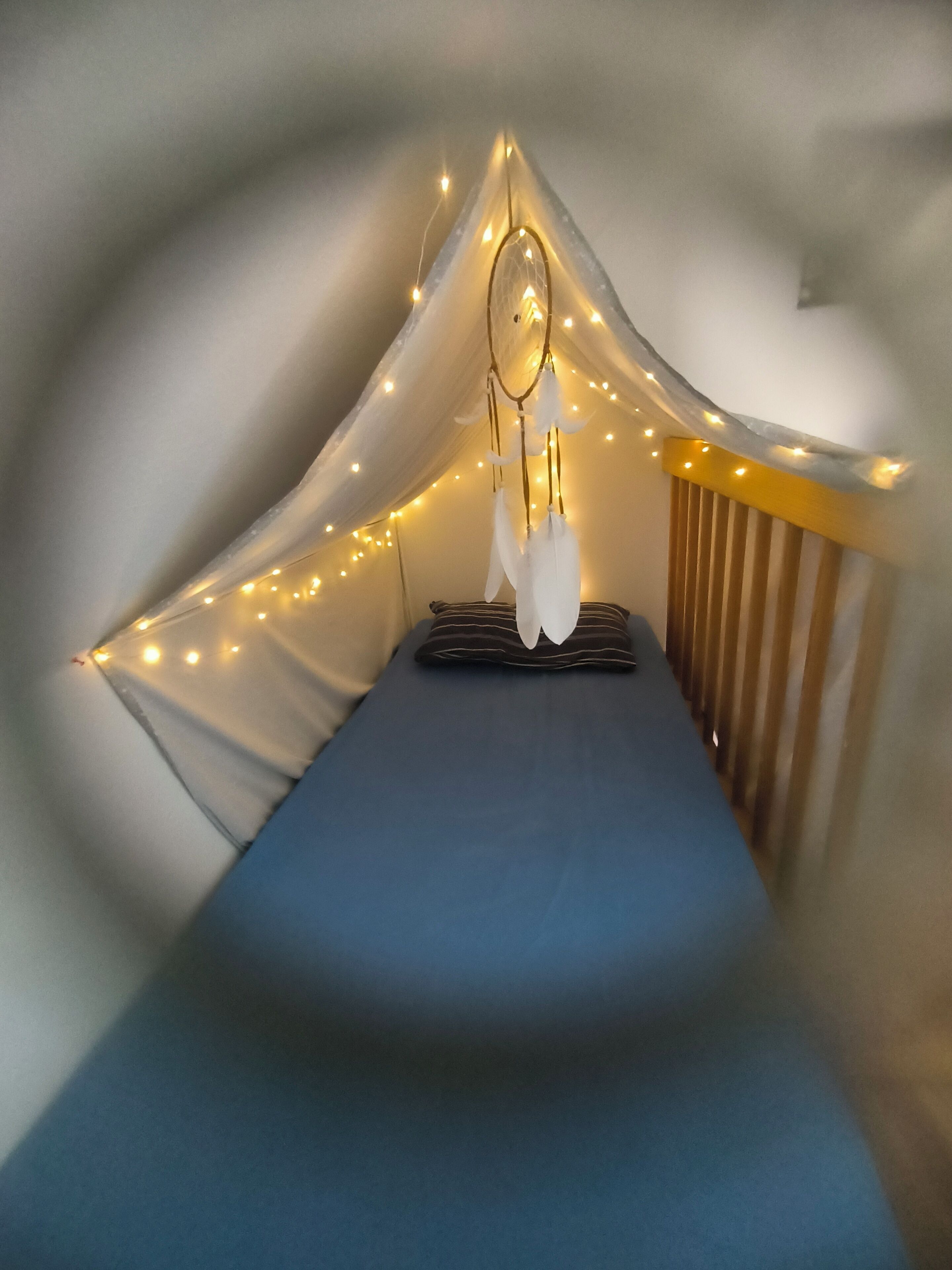 A tent-like room with a bed, string lights, and a hanging dreamcatcher.