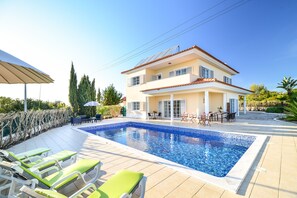 A two-story house with a swimming pool, outdoor seating, and a garden. - Spacious, modern villa with private swimming pool and sea view (Carvoeiro)