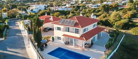 A two-story house with a swimming pool, solar panels, and a view of the surrounding neighborhood.