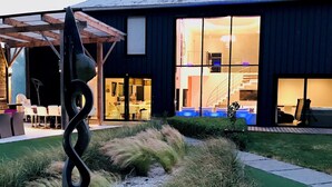 Un bâtiment moderne doté d’une grande entrée en verre, d’une sculpture en spirale en premier plan et d’un espace jardin bien entretenu.