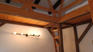 Una habitación con vigas de madera a la vista, techo inclinado y una lámpara fijada en la pared.
