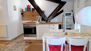 Una cocina con una mesa blanca, sillas y un microondas. Hay una alfombra en el suelo y un techo con vigas de madera.