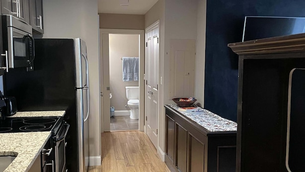 Una cocina moderna con electrodomésticos de acero inoxidable, suelo de madera y vistas al baño contiguo.