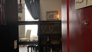 Una habitación con cama, candelabro, chimenea adornada con objetos decorativos y una puerta roja con un letrero.