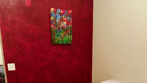 Una habitación con una colcha roja, un cuadro llamativo en la pared y un tapete a rayas.