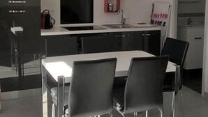 Een moderne keuken met zwarte kastjes, een wit aanrecht en een eethoek met een witte tafel en zwarte stoelen.
