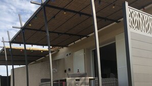 Een overdekt buitengebied met een pergola, rieten meubilair en een bord dat een restaurant aangeeft.