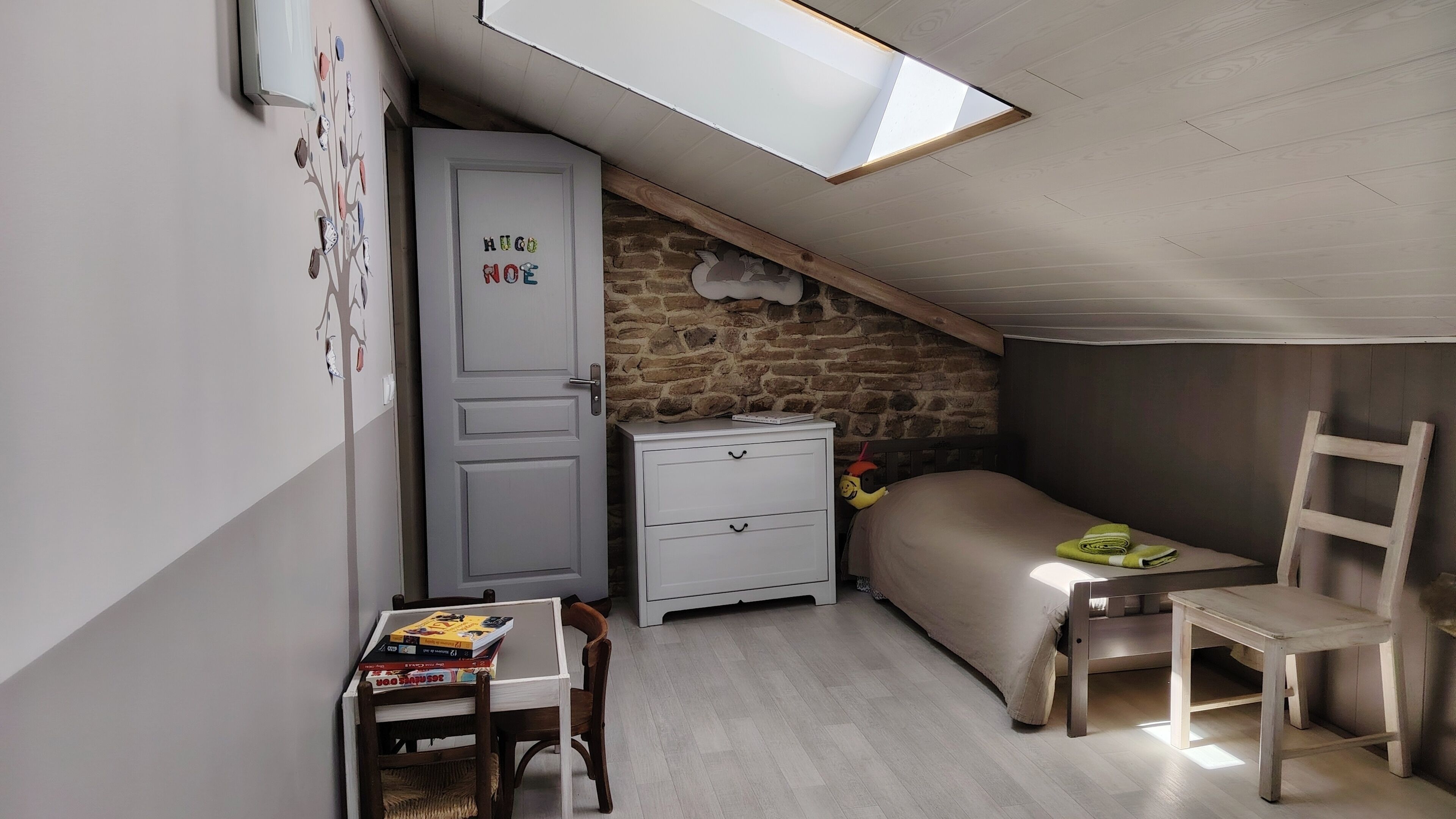 Une petite pièce agréable, avec un plafond en pente, un lit, un bureau avec une chaise, une armoire et une petite table.