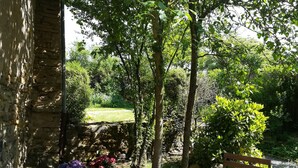 Una panchina di legno in un giardino con muri in pietra e vegetazione rigogliosa.