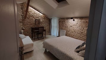 Ein Schlafzimmer mit Steinwand, einem Bett, einem Schreibtisch mit Stuhl und einer Heizung.