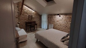 A bedroom with a stone wall, a bed, a desk with a chair, and a radiator. - Charm and nature near Cluny (Brandon)
