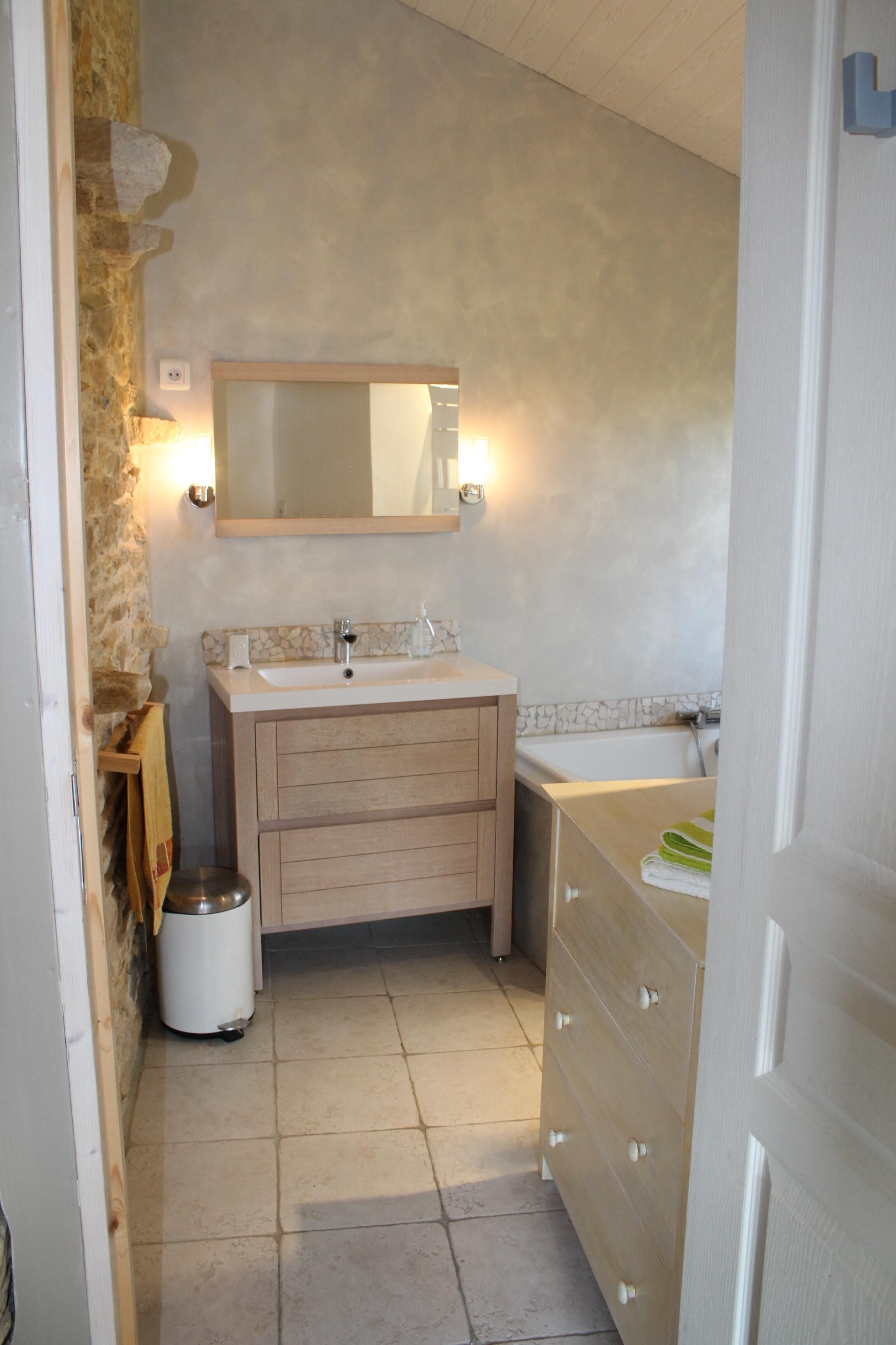 Une salle de bain avec un mur en pierre, un lavabo, un miroir et une baignoire.