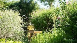 Un giardino con una panchina di legno, un muro in pietra e vegetazione lussureggiante.