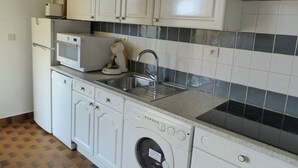 Una cocina compacta con armarios blancos, microondas integrado, cafetera, lavamanos y lavadora.