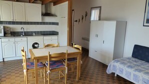 Una cocina compacta con armarios blancos, un fregadero y una estufa. Hay una mesa de comedor con sillas y una cama con colcha estampada.