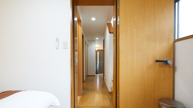 Un couloir d’hôtel avec un plancher en bois, un lit sur la gauche et une poubelle sur la droite.