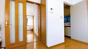 Un couloir doté d’un plancher en bois, une porte coulissante et un espace cuisine visible à travers une porte ouverte.