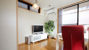 Un salon moderne avec un téléviseur à écran plat, un fauteuil rouge, une petite poubelle et une plante en pot.