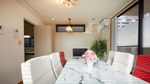Un coin repas avec une table en marbre, des chaises blanches rembourrées, un téléviseur à écran plat et une plante en pot.
