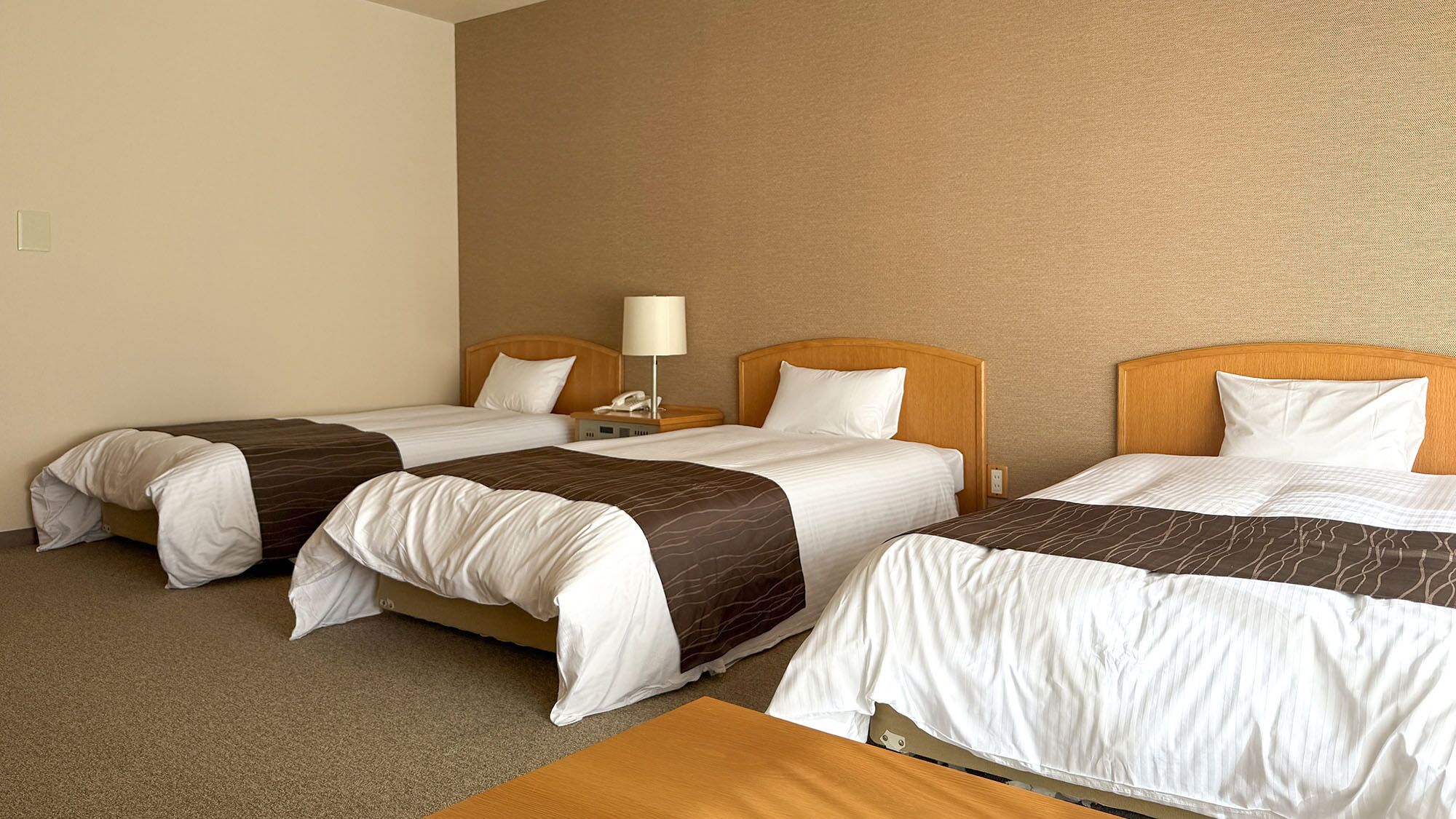 Habitación de hotel con dos camas individuales, una mesita de noche con lámpara y cabecero de madera.