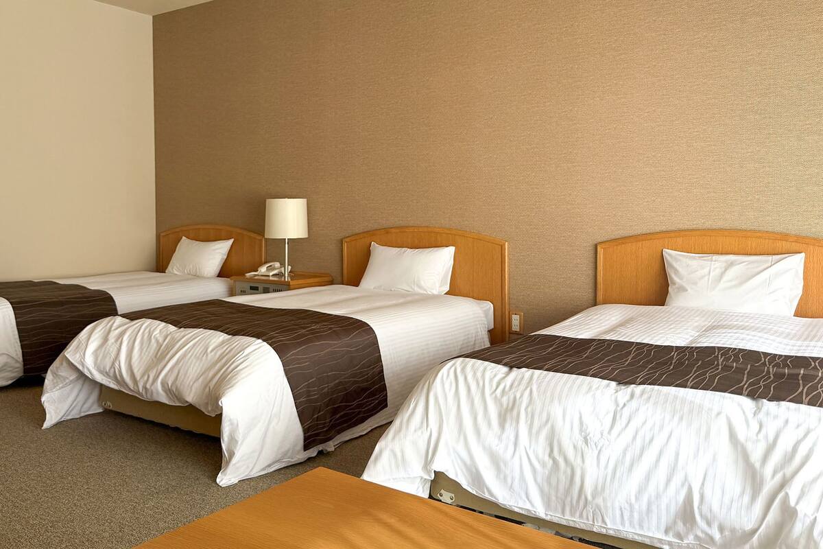 Habitación de hotel con dos camas individuales, una mesita de noche con lámpara y cabecero de madera.