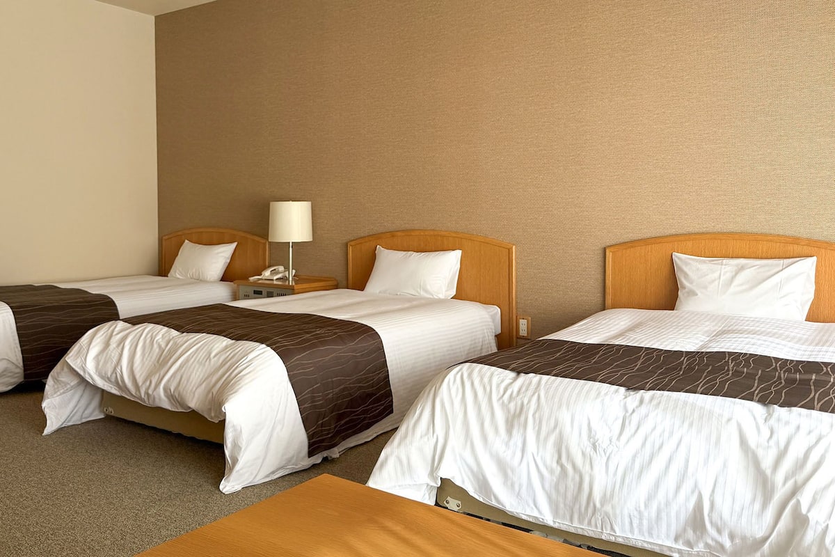 Habitación de hotel con dos camas individuales, una mesita de noche con lámpara y cabecero de madera.