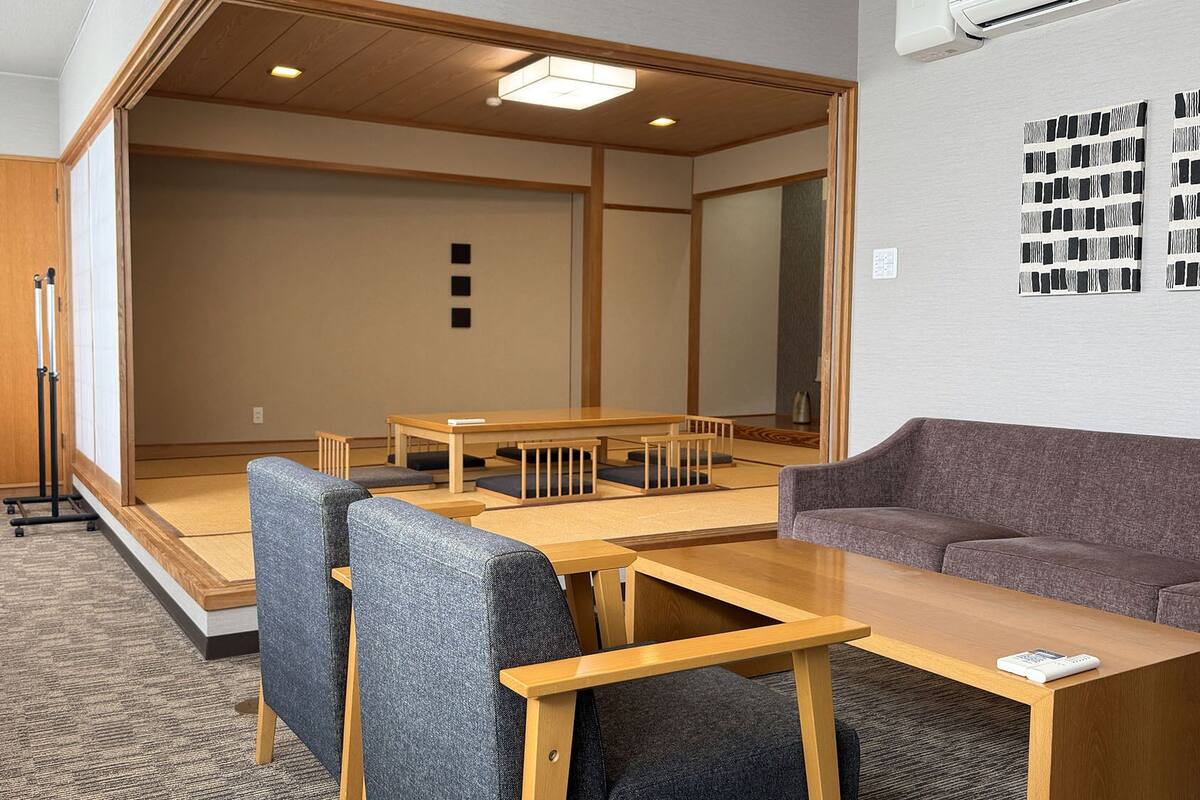 Una habitación con suelo de tatami, una mesa de madera baja, un sofá y una puerta corrediza tradicional japonesa.