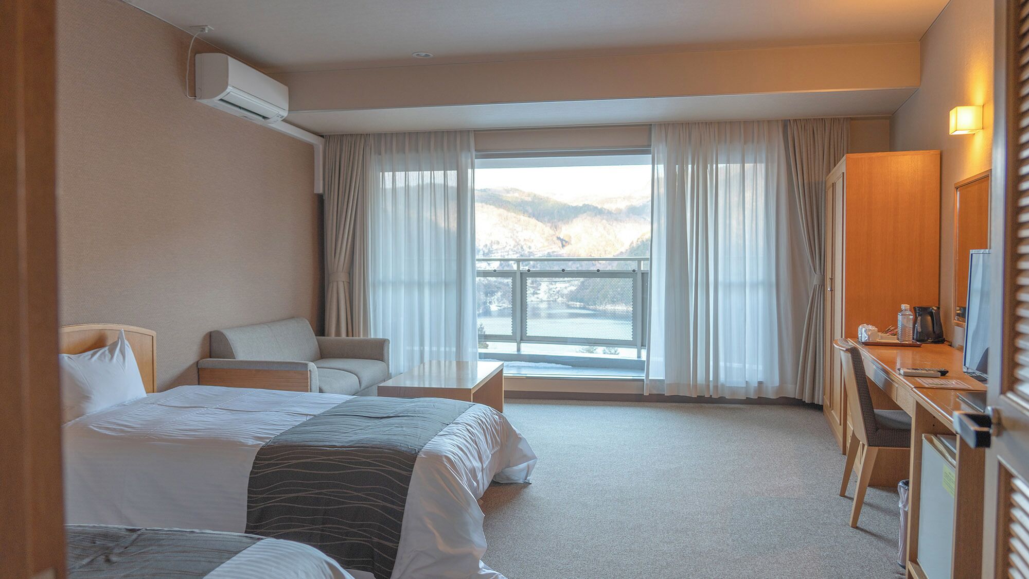 Quarto de hotel com cama, escrivaninha, cadeira e vista para uma varanda com montanhas.