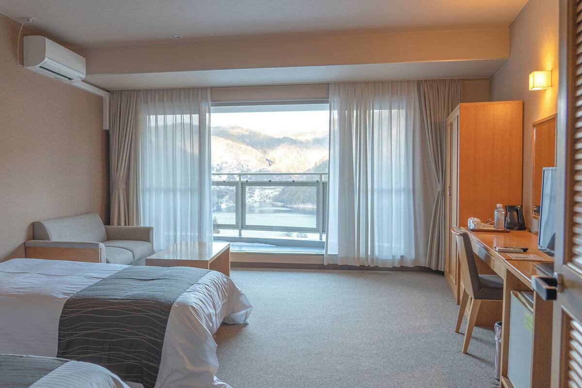 Habitación de hotel con cama, escritorio, silla y vistas a un balcón con montañas.