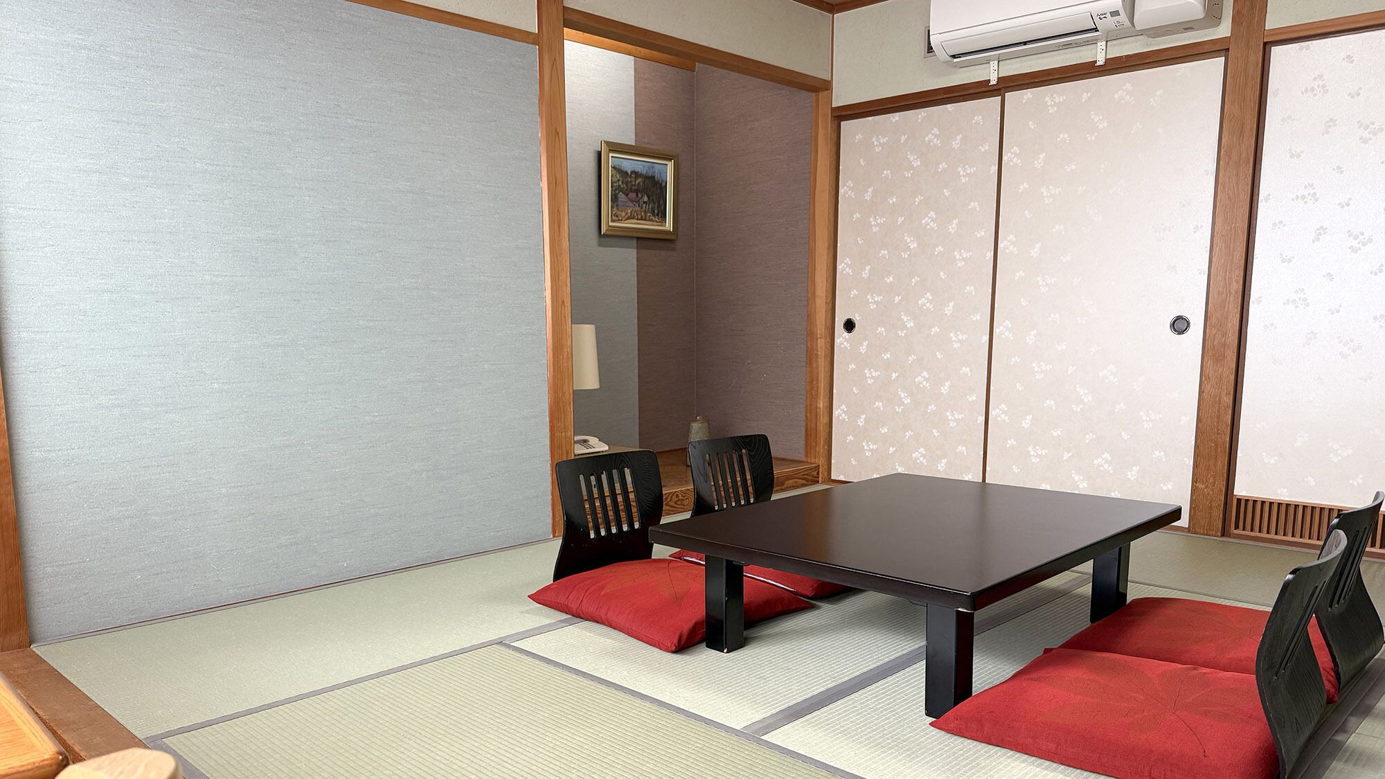Una habitación japonesa tradicional con suelo de tatami, una mesa baja y sillas negras con cojines rojos.