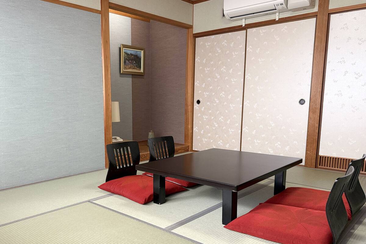 Una habitación japonesa tradicional con suelo de tatami, una mesa baja y sillas negras con cojines rojos.