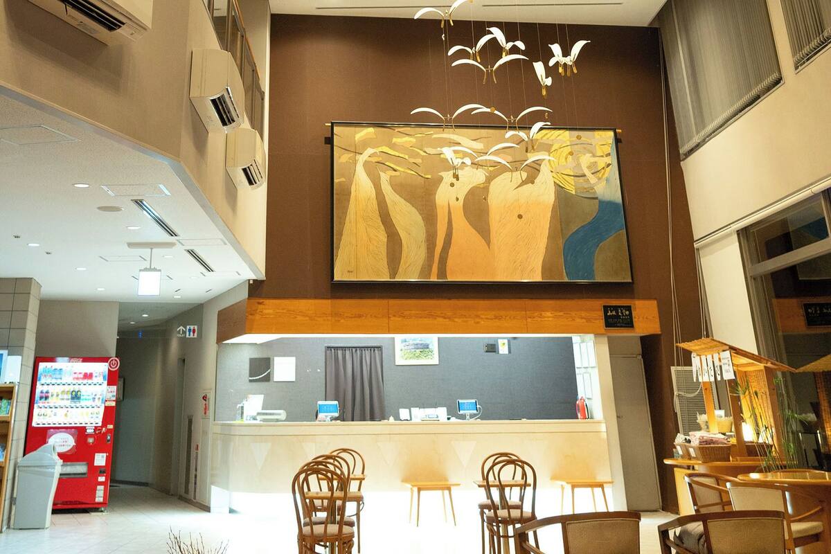 Un hall de hotel con mostrador de recepción, zona de estar, máquina expendedora y obras de arte en la pared.