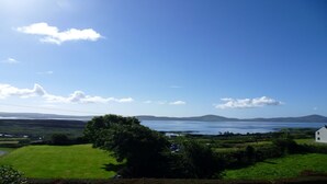 A rural landscape with a large body of water, hills in the distance, and a white building in the foreground. - Pine Cottage - Sheeps Head Peninsula (Bantry)