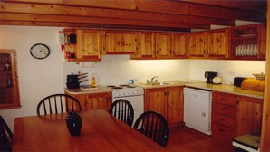 A compact kitchen with wooden cabinets, a stove, a sink, and a dishwasher. - Pine Cottage - Sheeps Head Peninsula (Bantry)