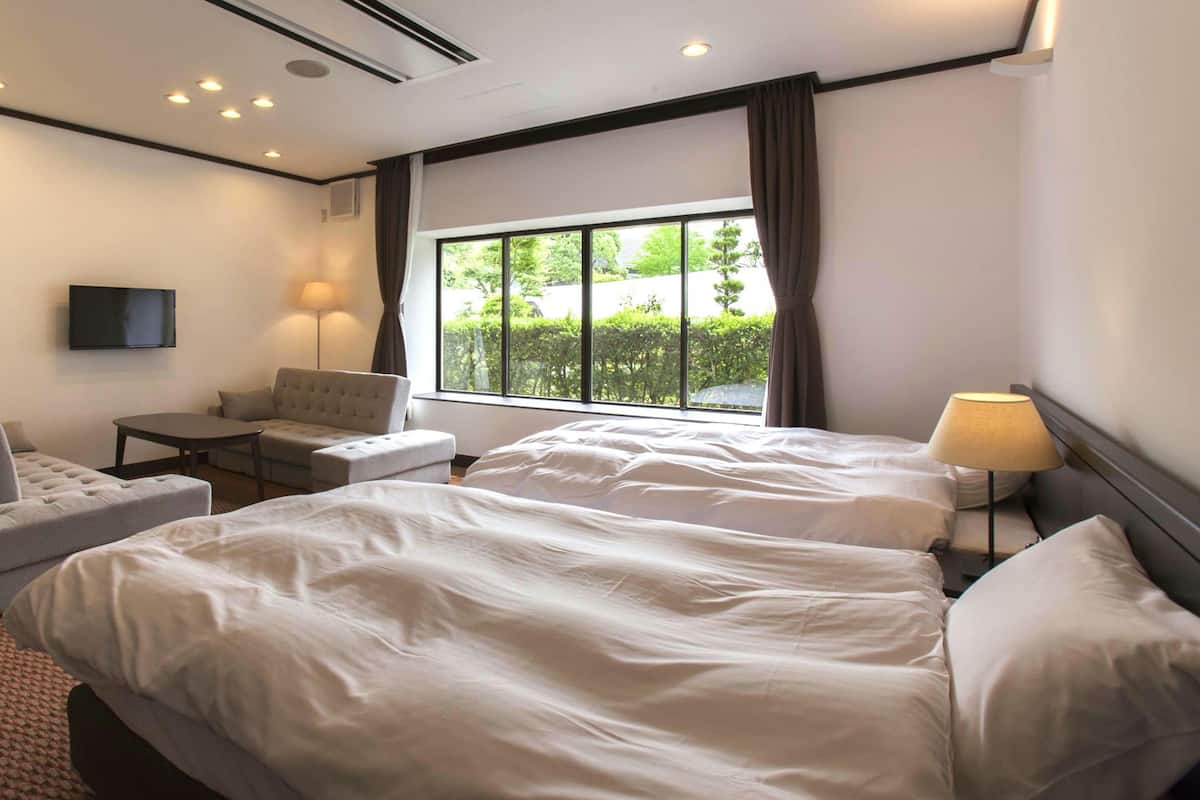 A hotel room with two beds, a sofa, a small table, a TV, and a window with curtains.