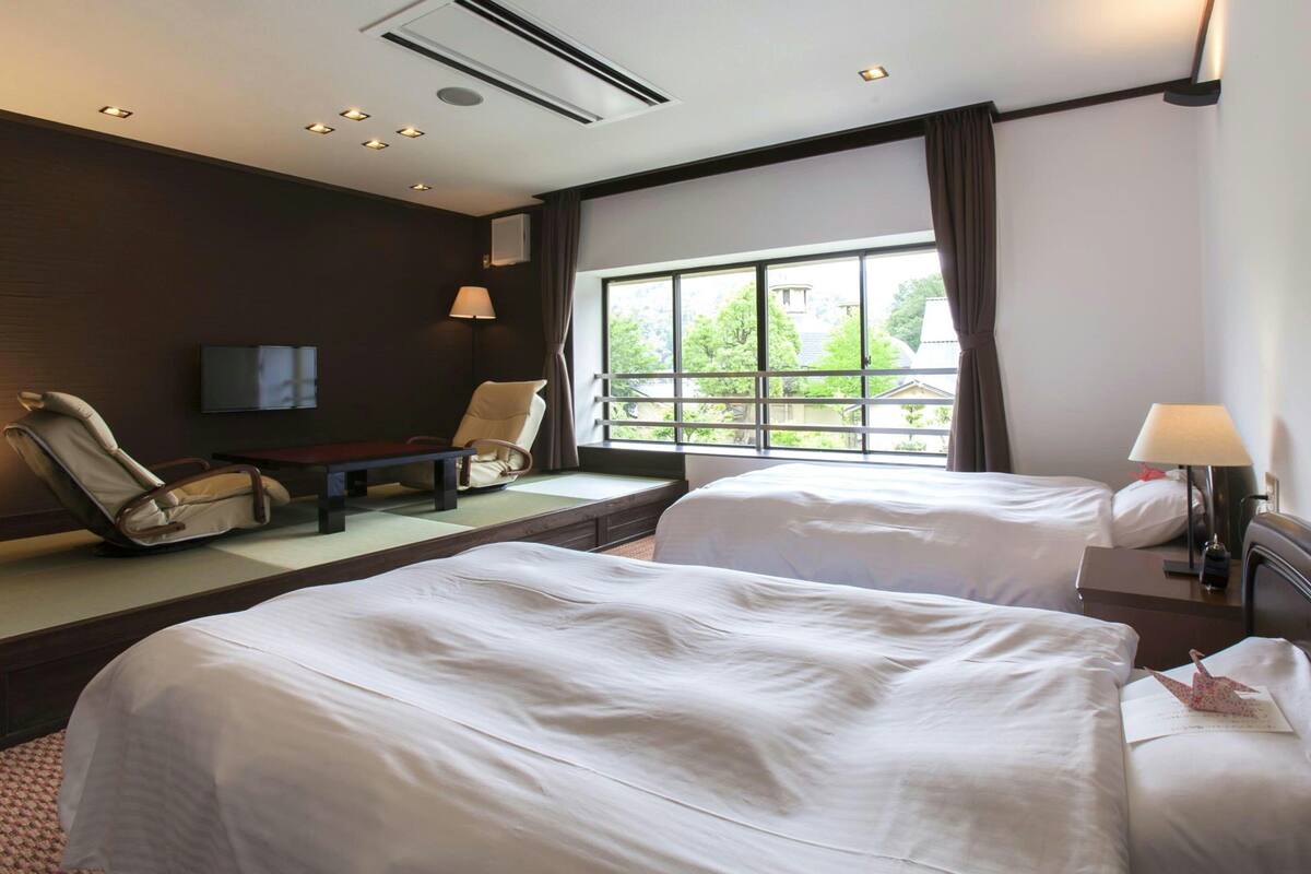 Ein Hotelzimmer mit zwei Betten, einem Sofa, einem Fernseher und einem Fenster mit Blick.