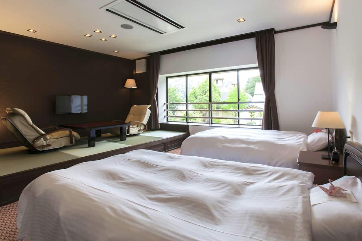 A hotel room with two beds, a sofa, a TV, and a window with a view.