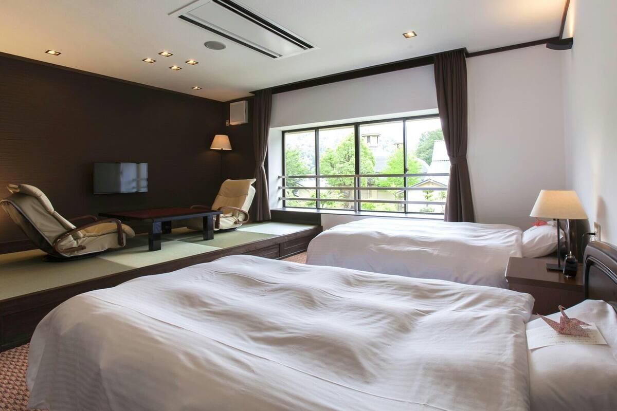 Ein Hotelzimmer mit zwei Betten, einem Sofa, einem Fernseher und einem Fenster mit Blick.