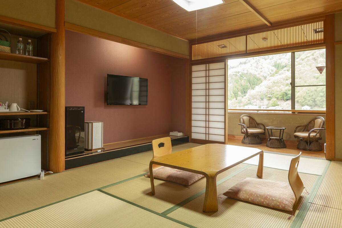 Ein traditioneller japanischer Raum mit Tatami-Böden, einem niedrigen Tisch und einem an der Wand befestigten Fernseher.