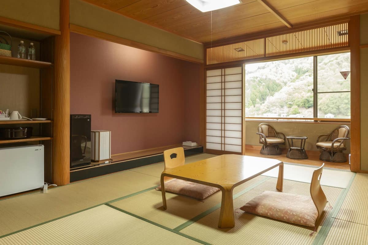 A traditional Japanese-style room with tatami flooring, a low table, and a television on the wall.
