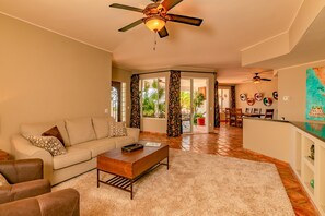 A spacious living room with a sofa, coffee table, and chairs, a wooden floor, and a ceiling fan.