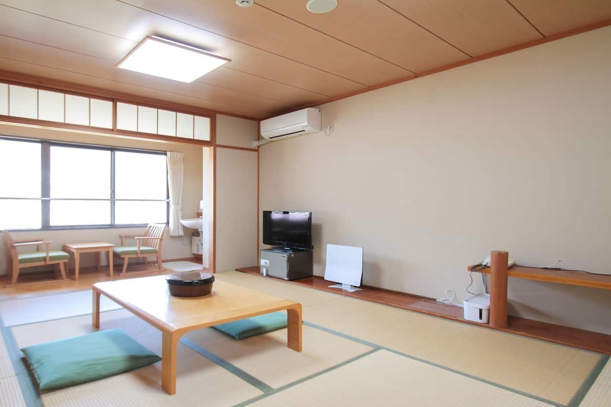 A traditional Japanese room with tatami flooring, a low table, a television, and a small refrigerator.