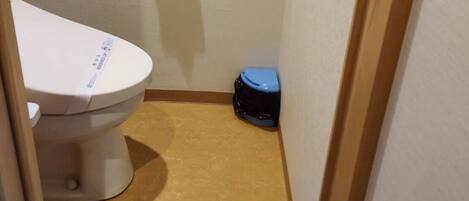 Un baño pequeño con un inodoro, un cubo de basura y un par de pantuflas en el suelo.