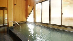 Een groot binnenzwembad met glazen wanden, houten lambrisering en een metalen trap die het water in leidt.