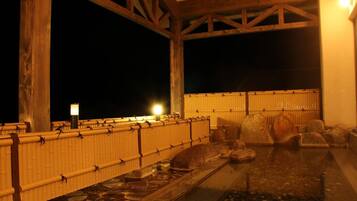 A traditional Japanese onsen with a wooden structure, a stone bath, and a bamboo fence.