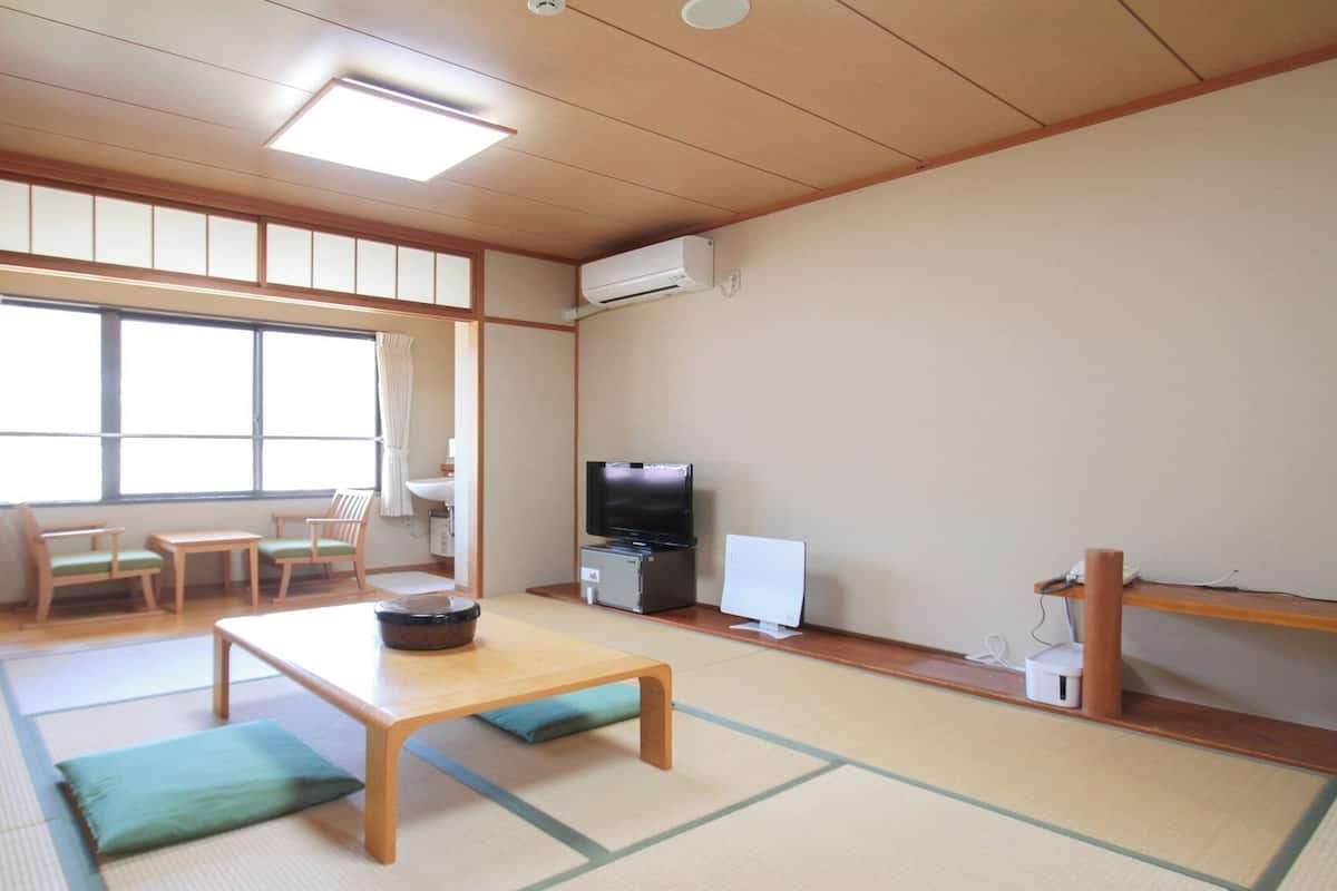 Ein traditioneller japanischer Raum mit Tatami-Boden, einem Fernseher, einem Kühlschrank und einem Holzregal.